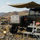 Jeep with rooftop tent and cooler in a desert setting with mountains.